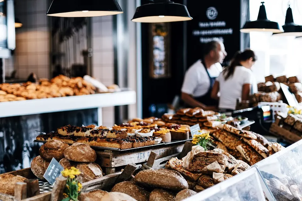 Comptoir d'une boulangerie garni de pains et de viennoiseries, deux employés en tablier derrière la vitrine